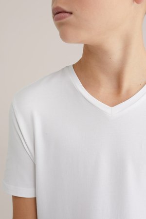 Fehér pamut póló V-nyakú kivitelben, rövid ujjakkal és sima textúrával. Közeli kép, amely a nyakkivágást és a vállrészt mutatja.