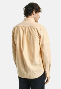 Gelb gestreifte Button-Up-Hemd aus weichem Stoff mit langen Ärmeln und abgerundetem Saum. Subtile weiße Streifen verleihen Textur und Muster.