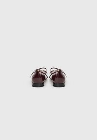 Bordeaux gepatineerde leren schoenen met een ronde neus, enkelbandje en kleine hak, voorzien van gouden hardwareaccenten op de bandjes.