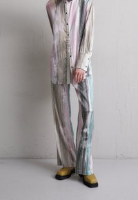 Pruhovaná košile a široké kalhoty v pastelových barvách s abstraktními vzory. Oblečení doplňují vysoce kontrastní žluté boty.