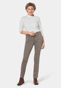 Bruine en crèmekleurige houndstooth-patroonbroek met twee zakken, gecombineerd met een witte lichtgewicht top en bruine veterschoenen.