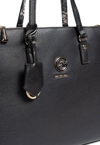 Sort læderhåndtaske med struktureret overflade, hardware i guldfarve, logoemblem og korte stropper. Inkluderer et aftageligt mærke på en ring.