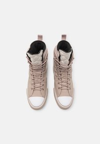 Vysoké tenisky z lehkého béžového kůže s bílými gumovými špičkami, s prošívanými detaily a béžovými tkaničkami. Součástí jsou také černé podšívky a poutka.