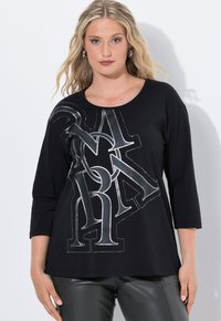 Schwarzes Langarm-T-Shirt mit einem großen silbernen Grafikdesign, das Buchstaben und Akzente enthält. Aus weichem Material mit einer lockeren Passform.