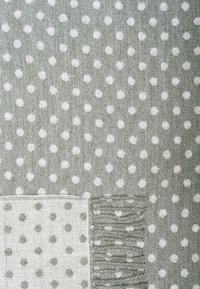 Tissu gris tissé avec des pois blancs et un coin plié montrant le motif inverse et un bord frangé.