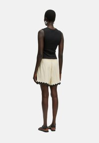 Zwarte mouwloze top in combinatie met crèmekleurige shorts met een geschulpte zwarte zoom. De outfit heeft een ontspannen pasvorm en een soepele textuur.
