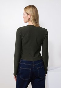 Mørk grønn ribbet langermet topp med rund hals, sammen med mørkeblå denimjeans med synlige sømmer og lomme detaljer.