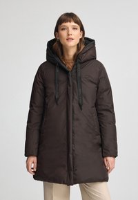 Brązowy ocieplany płaszcz z kapturem, z suwakiem z przodu, dwoma bocznymi kieszeniami i czarnymi sznurkami ściągającymi. Gładka tekstura i średnia długość.