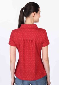 Red blouse with a collar, short sleeves, and a back pleat. Features a small floral pattern in lighter shades on a textured fabric.