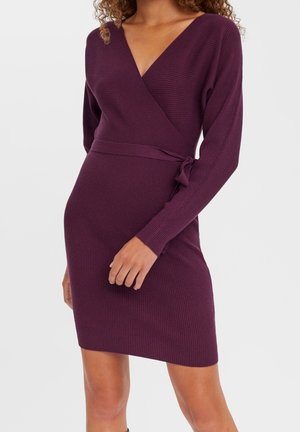 Vestido morado de manga larga con cuello en V profundo y tejido acanalado, cinturón en la cintura. El material es texturizado y ajustado, terminando por encima de la rodilla.