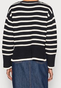 Randig stickad tröja i svart och vitt med en lös passform, ribbad textur och lätt rundad nederkant. Långa ärmar med en kontrasterande nederkant.