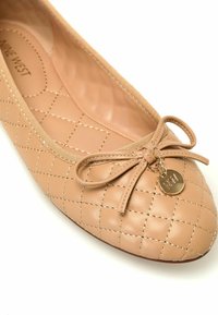 Beige gewatteerde balletschoen met een ronde neus, voorzien van een strik en een gouden charm aan de voorkant, gemaakt van soepel synthetisch materiaal.