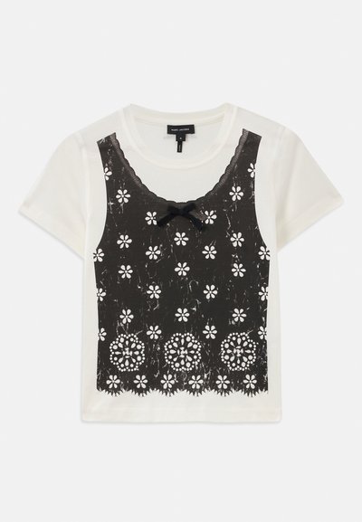 Witte t-shirt met korte mouwen, voorzien van een zwarte kanten bloemenOverlay, een scalloped halslijn en een strikaccent in het midden.