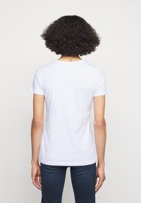 Vit bomullst-shirt med korta ärmar, rundad halsringning och en sömdetalj på baksidan. Bärs med mörkblå jeans, visas från baksidan.