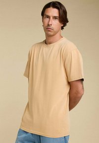 T-shirt en coton beige à manches courtes, col rond et coupe droite. Présente un logo de marque subtil à l'ourlet.