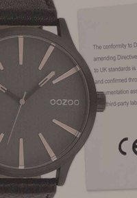 Montre analogique noire avec finition mate, cadran minimaliste, index horaires en argent, et bracelet en cuir noir. Comprend un label de conformité CE.