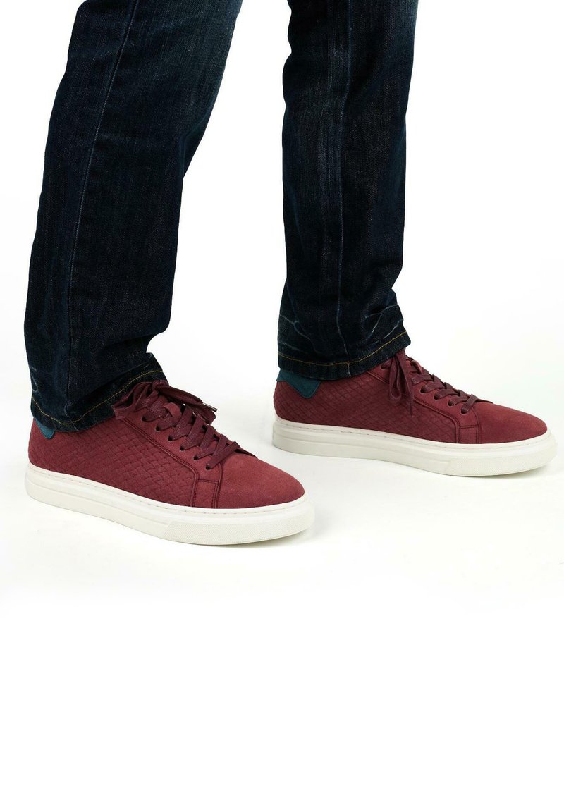 Rode suède sneakers met een gestructureerd patroon en een witte rubberen zool, gecombineerd met donkerdenim jeans. Bevat platte veters en contrasterende blauwe accenten.