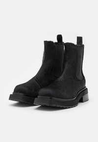 Svarta chelsea-boots i texturerat, hårigt material, med elastiska sidor och dragflikar, samt en robust och hållbar sula.