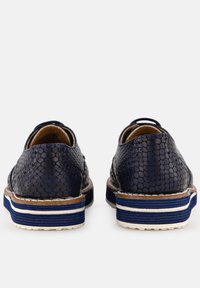 Pár tmavě modrých bot z umělé hadí kůže se bílými a modrými pruhovanými podrážkami, zobrazených ze zadní strany na bílém pozadí.