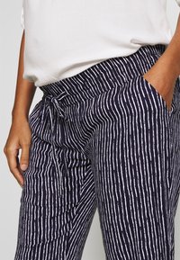 Navy pants with white vertical stripes, featuring an elastic waist, drawstring closure, and side pockets, showcasing a lightweight fabric texture.