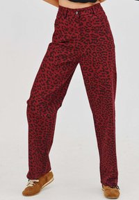 Nohavice s potlačou červeného leoparda majú vysoký pás, rovný strih a klasické zapínanie na gombík, vyrobené z hladkej zmesy bavlny.