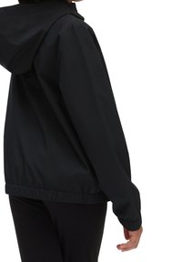 Black lightweight jacket with a hood, elastic cuffs, and a gathered hem. Smooth texture with a simple, minimalist design.