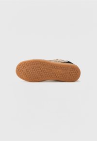 Semelle de sneaker noire et dorée avec une surface texturée en caoutchouc et un motif en nid d'abeille. Accentuée de détails métalliques sur la partie supérieure.