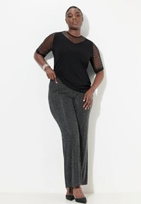 Zwarte top met doorschijnende gestipte mouwen, gecombineerd met zwart en zilver gestreepte wijde broekspijpen. Glad materiaal met een relaxte pasvorm. Geen zichtbare patronen.