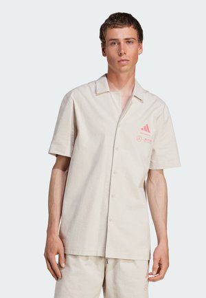 Short-sleeve, cream-colored button-up shirt made of textured fabric, featuring a pink logo and branding detail on the left side.