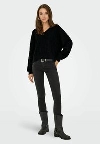Pull noir en tricot avec un décolleté en V et un motif texturé, associé à un jean noir ajusté et des bottes montantes noires avec un détail de boucle.