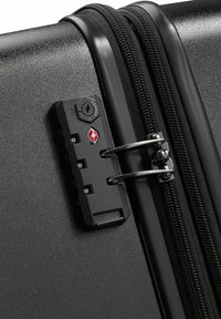 Angolo di una valigia rigida nera con lucchetto a combinazione, meccanismo con cerniera e hardware argentato. La superficie presenta una finitura testurizzata.