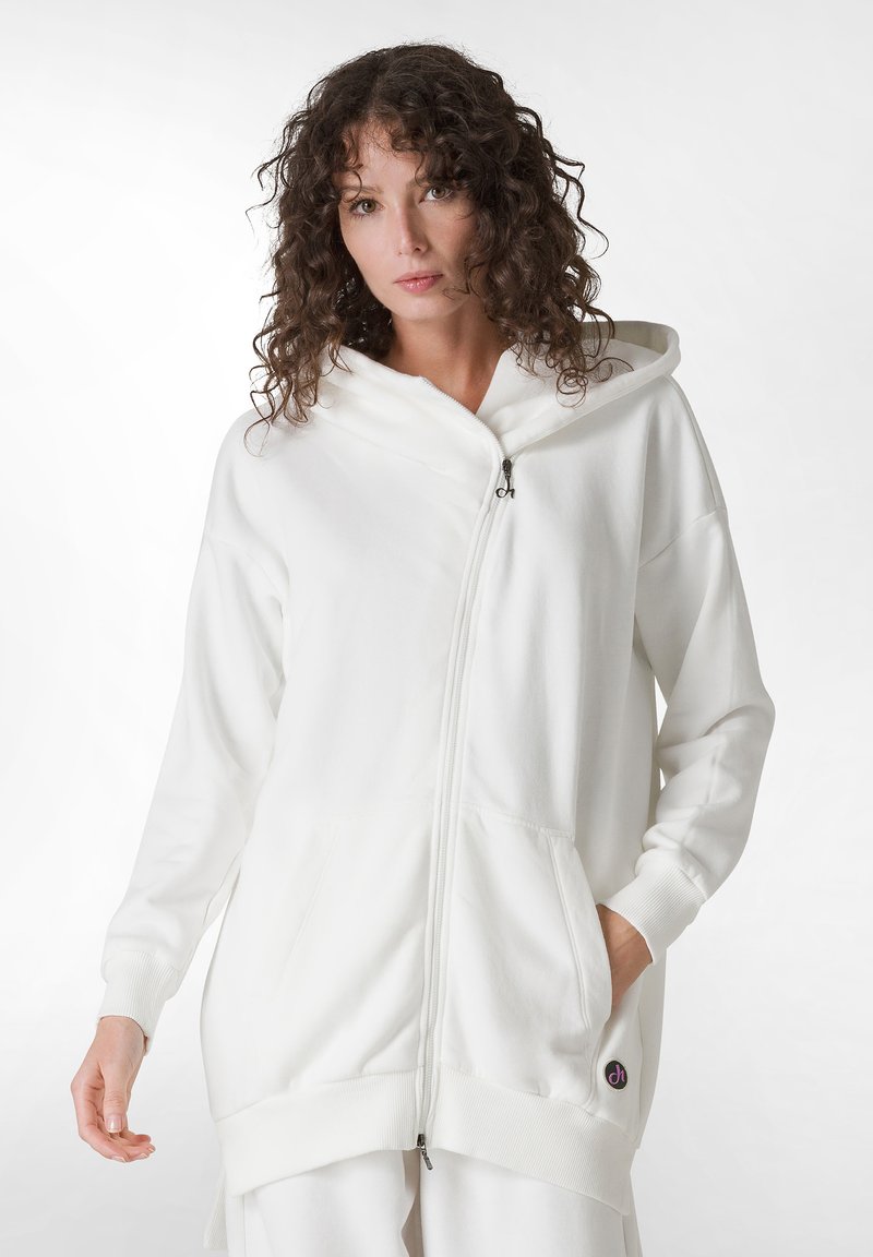 Sudadera de cremallera blanca hecha de un tejido suave, con capucha, bolsillos laterales, puños acanalados y un parche de logo en el costado inferior.