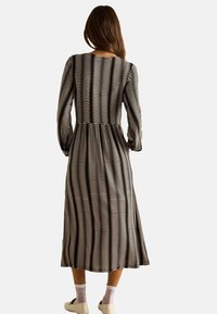 Vestido negro de manga larga con un patrón de olas blancas, una cintura entallada y una falda acampanada, hecho de una tela suave. Combinado con zapatos blancos.