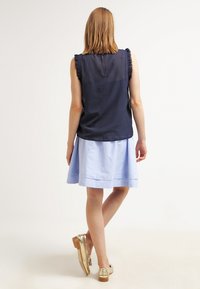 Mörkblå ärmlös topp med volangdetaljer på axlarna, i kombination med en ljusblå A-linjeformad kjol och metallicguldskor. Släta tygtexturer.