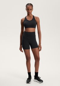 Črna športna modrček in kratke hlače z visokim pasom iz raztegljivega, vlago vpijajočega materiala. Ima preprost dizajn in prilegljivo silhueto.