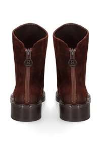 Bruine suède enkelboots met een ritssluiting, ronde neus en een lage houten hak versierd met metalen studs rondom de basis.