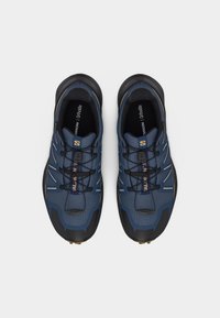 Ζευγάρι μπλε και μαύρα παπούτσια trail running της Salomon με κορδόνια γρήγορου τραβήγματος, σε θέα από πάνω σε απλό λευκό φόντο.