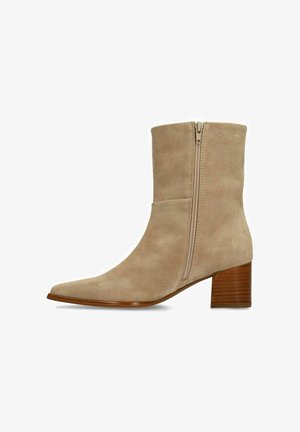 Bottine en daim beige avec un bout pointu, une fermeture éclair latérale et un talon en bois empilé. Texture lisse et silhouette élégante.