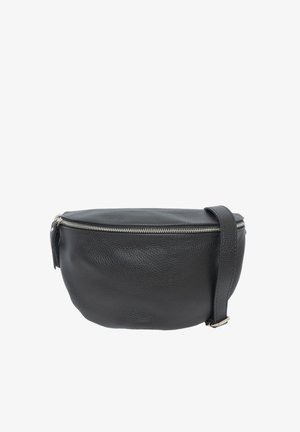 Jeune femme aux longs cheveux bruns, portant un haut noir à manches longues et un pantalon en cuir, avec un grand sac bandoulière en cuir noir.