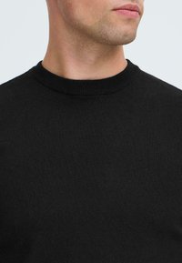 Zwarte crewneck trui van een glad gebreide stof. Kenmerkt zich door een geribbelde halslijn en een naadloos ontwerp, wat zorgt voor een schone, minimalistische uitstraling.