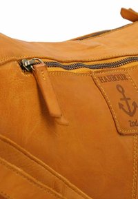 Borsa in pelle testa di moro con finitura testurizzata, dotata di chiusura con zip e di una patch con il logo di un'ancora. Cuciture e dettagli hardware a vista.