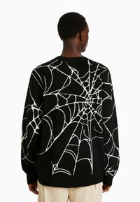 Svart tröja med ett vitt spindelnätdesign, tillverkad av ett mjukt material med avslappnad passform och ribbat halslinning.