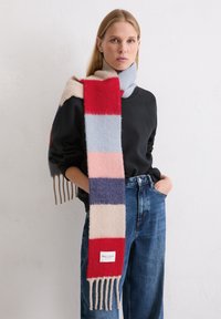 Wool scarf with horizontal stripes in red, pink, blue, and navy. Features fringe edges and a brand label at the bottom.