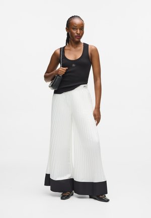 Czarny top na ramiączkach, białe szerokie spodnie z fałdami i czarnym wykończeniem, oraz czarna torebka. Całość dopełniają płaskie buty.