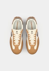 Béžové a krémové tenisky se šněrováním, vyrobené z semiše a tkaniny. Logo na boku, texturovaná gumová podrážka.