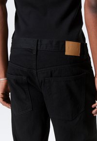 Sorte denimjeans med en lærmerke på baksiden, to stikrede baklommer og en teksturert stofffinish.