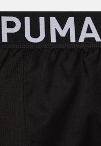 Mustad mustad spordihooled elastse vöökohaga, millel on valge "PUMA" bränd. Materjal on siledat tekstuuri ning kergelt läikiv ja kogutud.