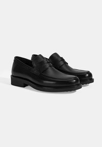 Schwarze Lederloafers mit glatter Oberfläche, runder Spitze und einem dekorativen Riemen über dem Fußrücken. Die dicke Gummisohle sorgt für Traktion.
