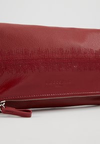 Červená kožená taštička s texturovaným povrchem, s lesklým vzorem, embosovaným logem a kovovým zipem s textilním táhlem.