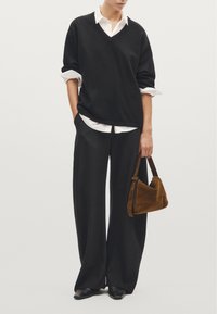 Black oversized sweater with V-neck, white shirt collar underneath, wide black trousers, and a small brown suede handbag. Black pointed flats.